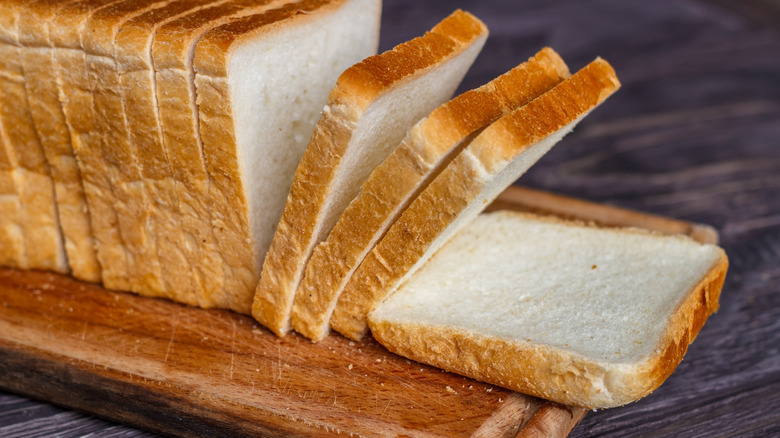 Pre-sliced loaf of white bread on cutting board