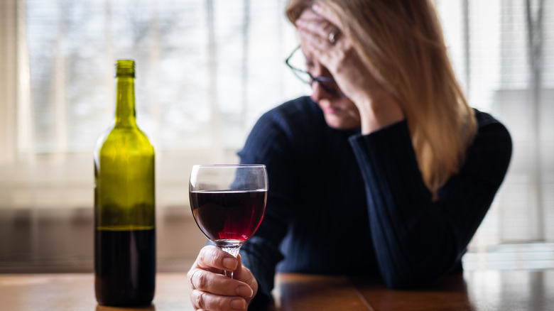 Person holding their head with a glass of wine in hand