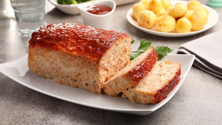 Meatloaf on dish with potatoes and ketchup in the background.