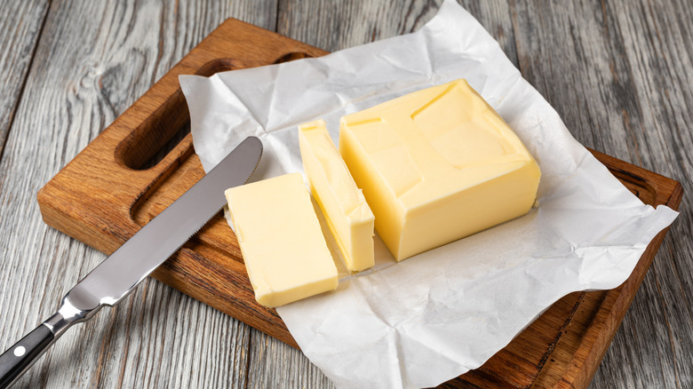 Butter and knife on wooden board.