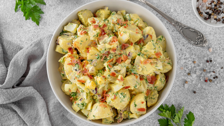 A bowl of potato salad topped with bacon bits on a table
