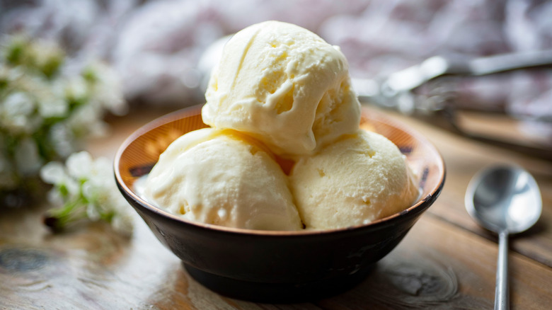 Three scoops of ice cream in a wooden bowl on a table.