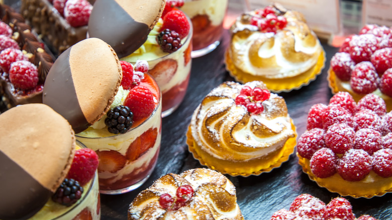 Aerial view of a variety of colorful desserts with whipped frosting, berries, cookies and powdered sugar, all on a dark table.
