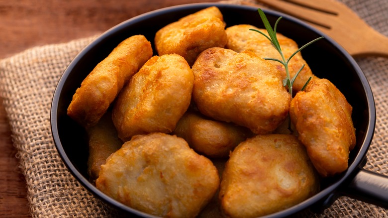 Homemade chicken nuggets in a frying pan with a sprig of rosemary on a burlap cloth