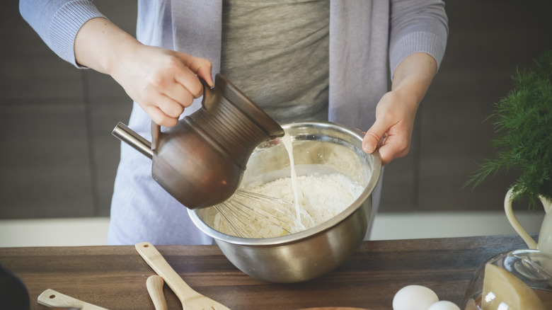 Person pouring milk into a bowl of flour