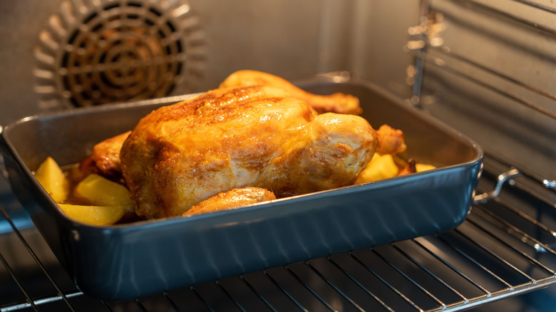 A chicken roasting in the oven with potatoes