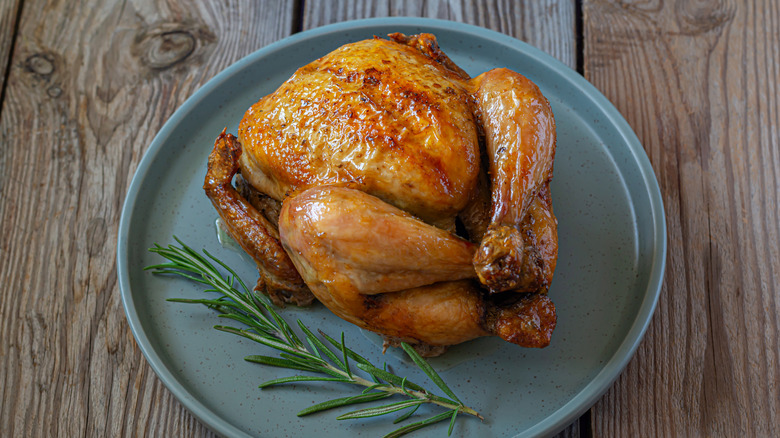 A roast chicken with a sprig of rosemary on a blue plate