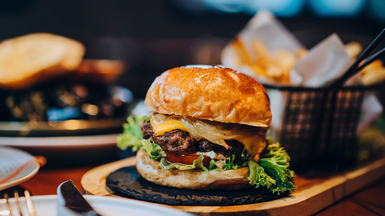 A burger topped with caramelized onions and melty cheddar cheese and a basket of fries sit on a table at a restaurant