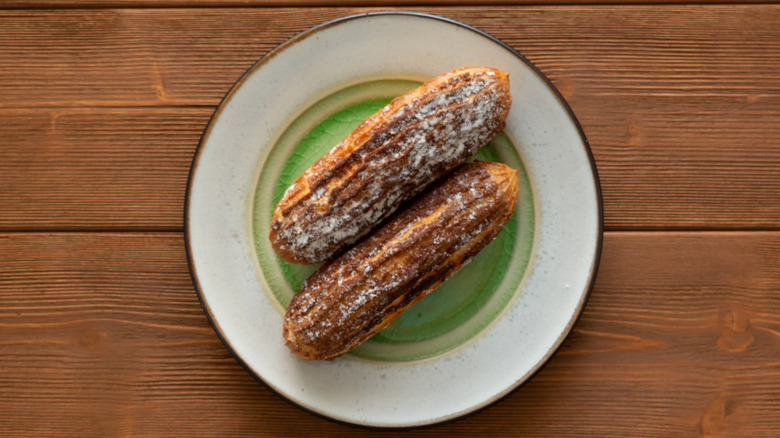 Two eclairs frosted with sugar sit on a plate with a green circle.