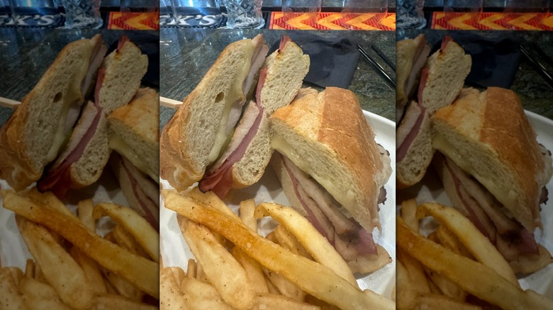 Halved Cubano displaying meat and cheese served beside a plate of French fries