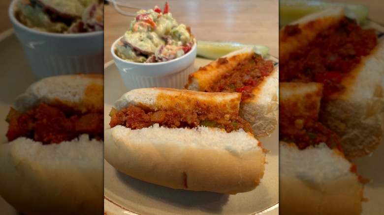 Ground beef with tomato sauce, onions, and peppers on a roll plated with slaw and a pickle