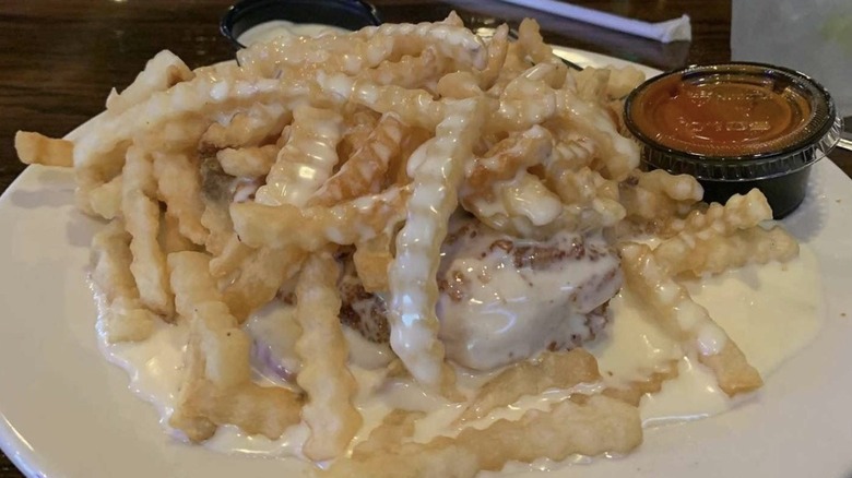 Cheese smothered fries covering a sandwich plated on a bar counter