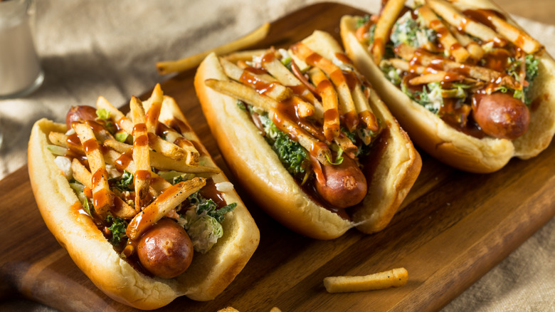 Trio of Polish boy's topped with fries, slaw, and sauce on a board