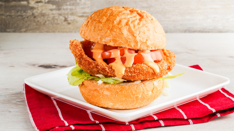 Thick bun holding a bread pork chop with tomato, lettuce, and dressing on a plate