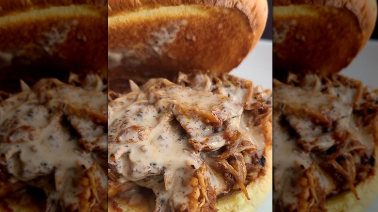Toasted bun propped open to show pulled chicken smothered in white sauce