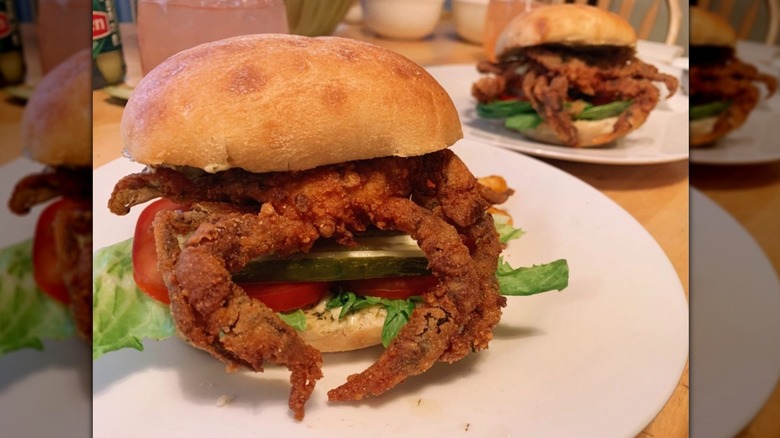 Breaded and fried soft shell crabs atop buns with pickle, tomato, and lettuce