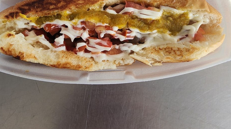 Bacon-wrapped Sonoran hot dog on a toasted bun with various toppings