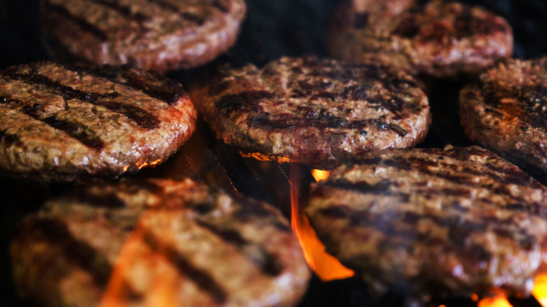 Hamburger patties are flame-cooked on a grill