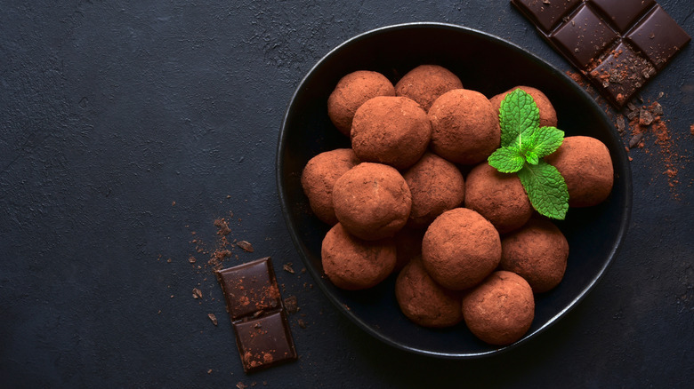 Chocolate truffles in a black bowl with a mint sprig and a few dark chocolate blocks near the bowl