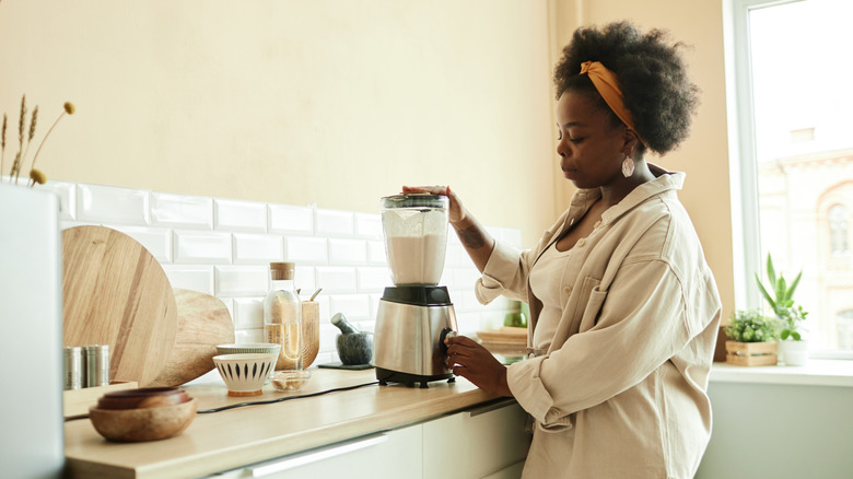 A stylish but casual person blending a milkshake in the kitchen