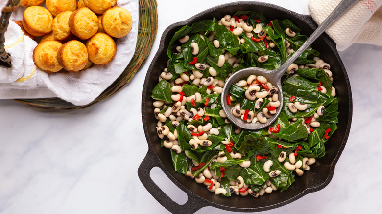 Black eyed peas, collard greens, red bell peppers in cast iron pot with ladle, cornbread muffins