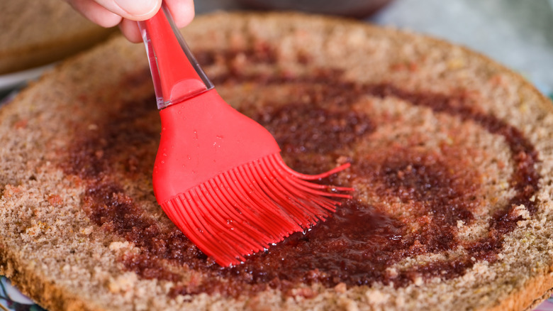 Person burshing sponge cake with cherry syrup