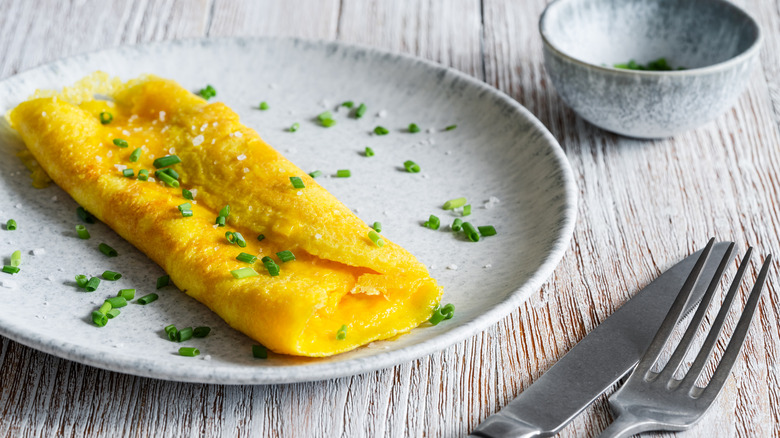 French omelet with chives on plate with fork and knife.