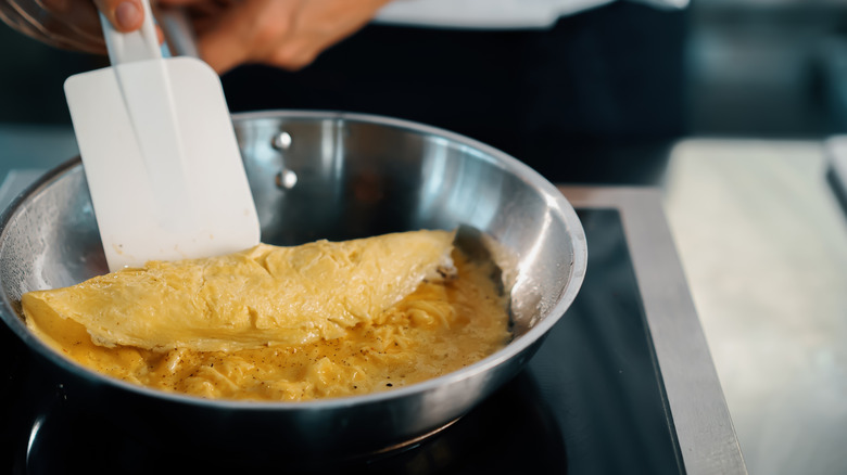 Person folding over French omelet in pan.