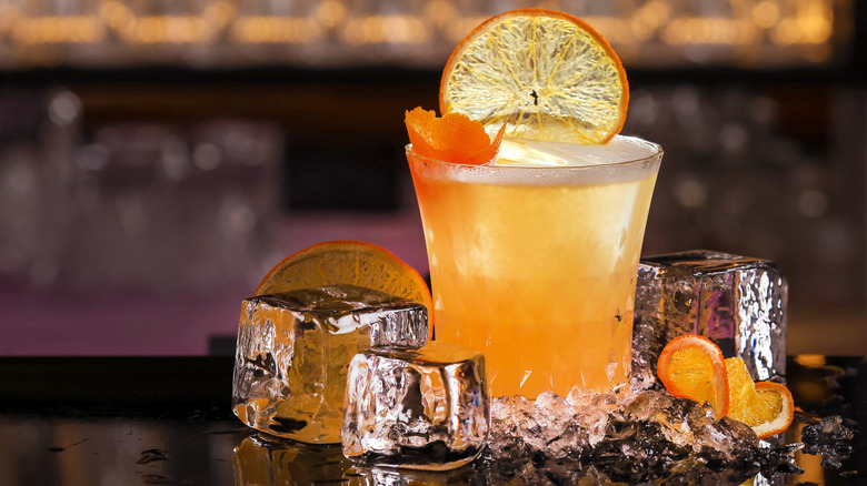 Whiskey sour with slices of orange and ice cubes on bar top