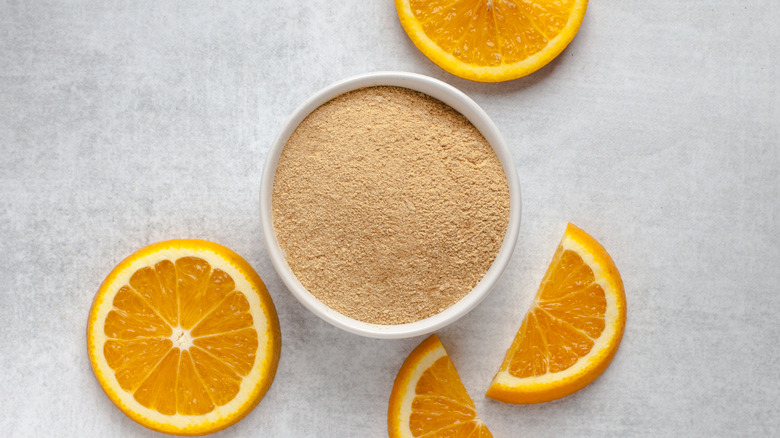 Orange peel powder in a small bowl, with a few orange slices around it