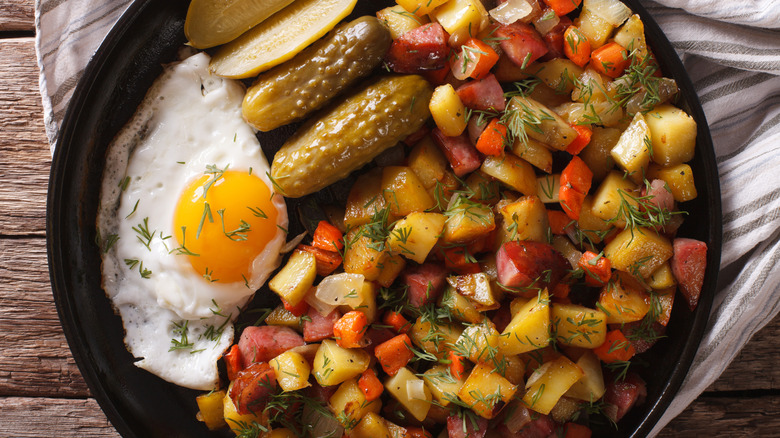 Hash made with veggies, potatoes, sausages, pickles, and eggs.