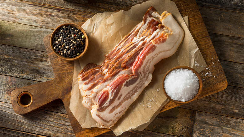 Uncured bacon on a wooden cutting board with salt and pepper