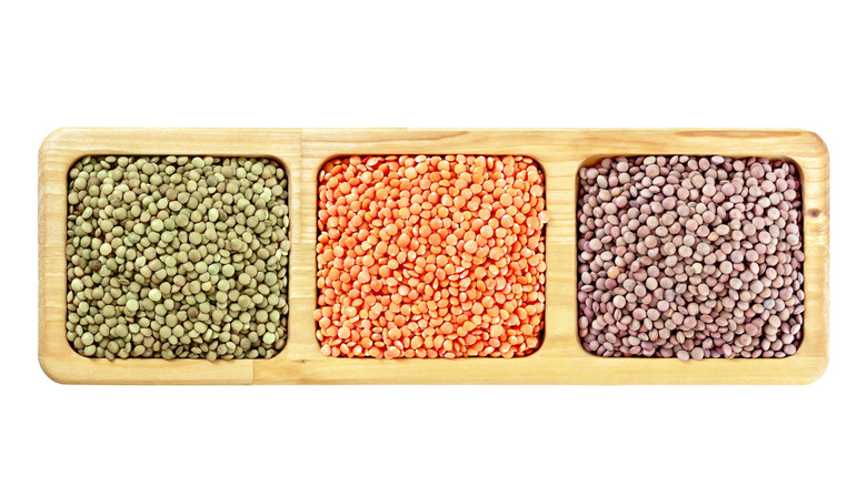 green, red, and brown lentils in a wooden holder