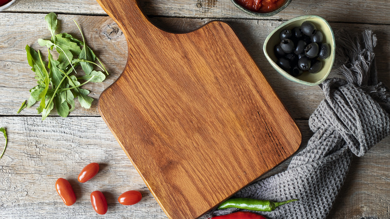 A wooden cutting board sits on a table surrounded by ingredients