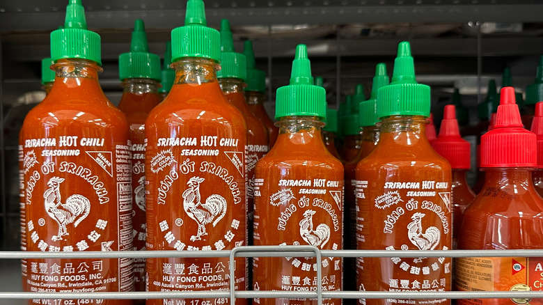 Bottes of red sriracha sauce with green caps in rows