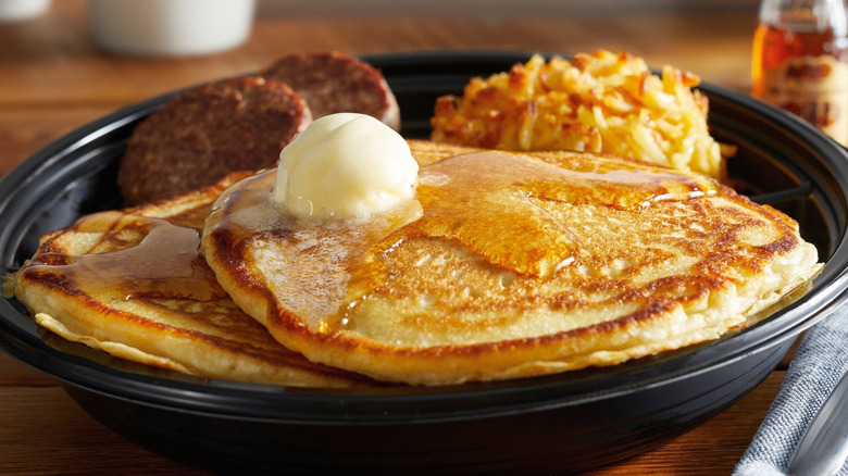 A plate of Cracker Barrel pancakes with hash browns and meat.