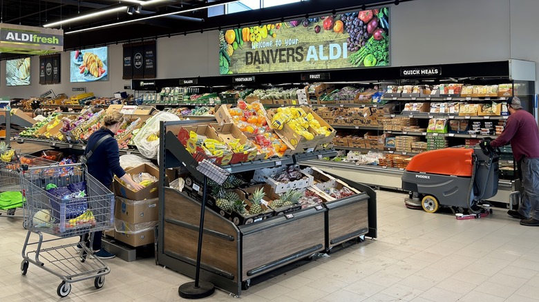 The inside of a grocery section of an Aldi, shoppers with carts stroll along the aisles