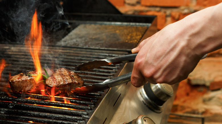 Hand flipping steaks on a grill with tongs