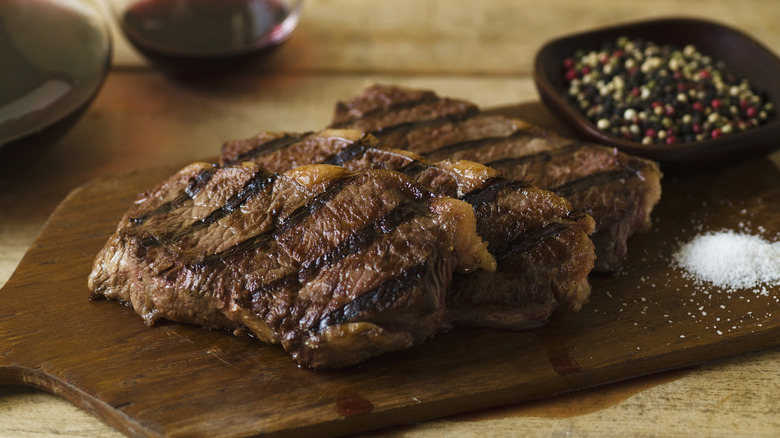 Steak on a wooden serving board with salt and spices
