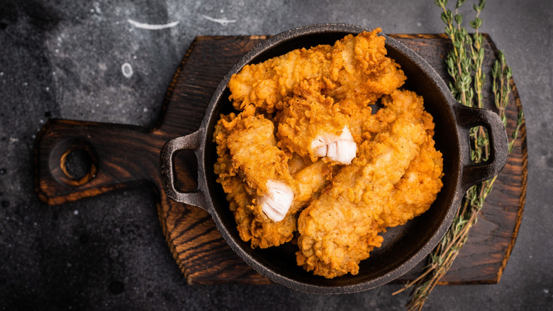 A metal pot of fried chicken tenders on a wooden board