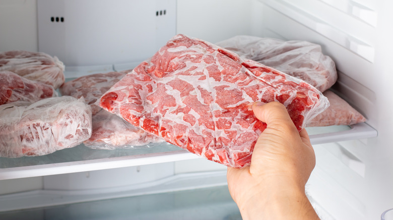 A hand reaches into a freezer to grab a ziploc bag full of frozen ground beef