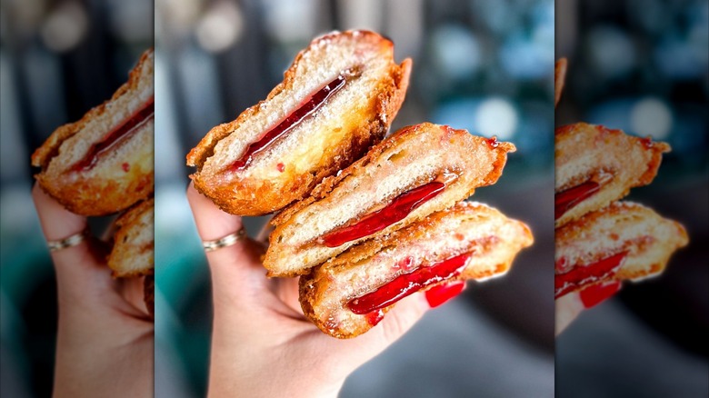 A handwith long red nails holds three deep fried Uncrustables