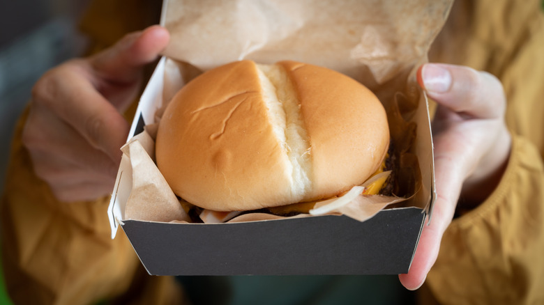 A woman holds a Jack in the Box burger placed in a cardboard box lined with parchment paper