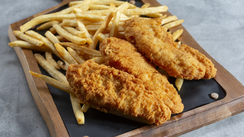 Chicken tenders on a wooden tray with french fries
