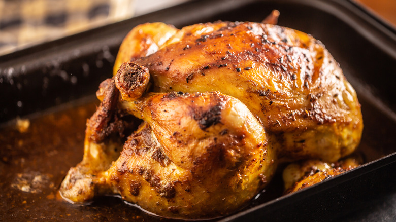 A whole roasted chicken on a oven tray sitting in oil