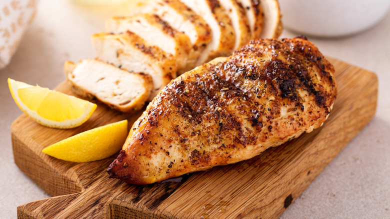 Chicken breast on a wooden tray with lemon wedges