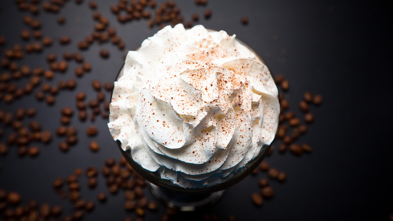 whipped cream on coffee with coffee beans in background