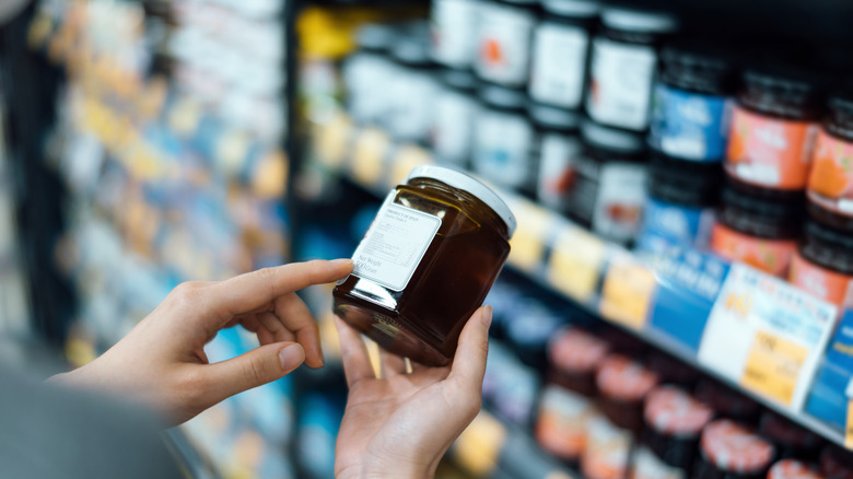 hands holding jar of jam in grocery store