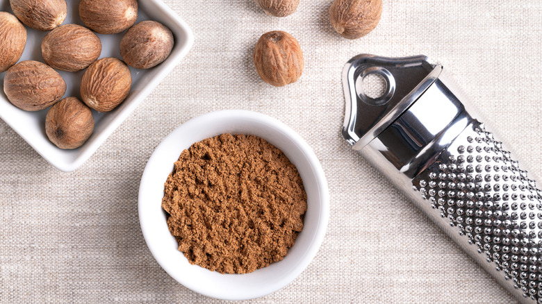 Whole and ground nutmeg pieces next to a grater on a tablecloth
