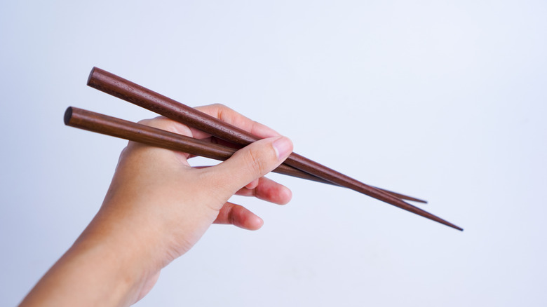 A person holding brown wooden chopsticks.